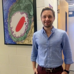 Luke Kaplan standing in front of red blood cell EM image, colorized